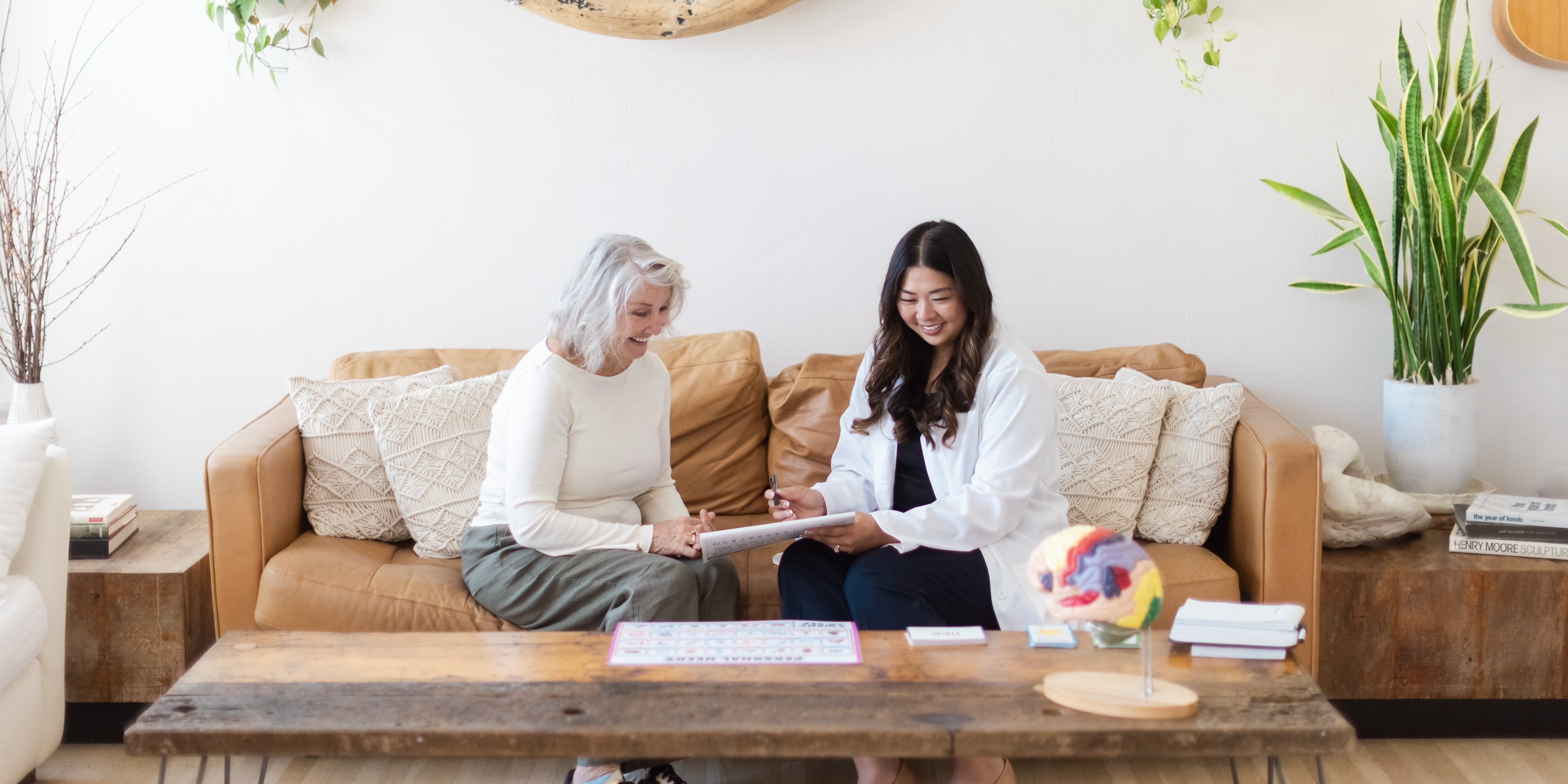Speech-language pathologist and a client smiling as they review therapy materials together on a sofa